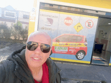 a man wearing sunglasses is standing in front of a building that says credenciado pare auto escola vidal