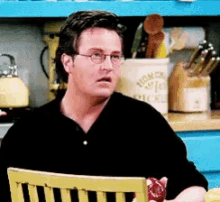 a man wearing glasses sits in a chair in front of a kitchen shelf that has a container that says home