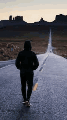 a man is walking down a long road with mountains in the background .