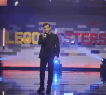 a man in a suit stands on a stage in front of a sign that says lego masters