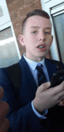 a young boy in a suit and tie is holding a cell phone