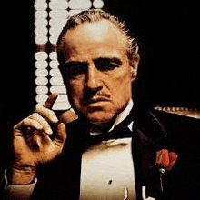 a man in a tuxedo is smoking a cigar and looking at the camera .