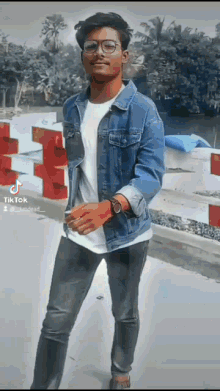 a young man wearing glasses and a denim jacket is standing in front of a red and white staircase ..