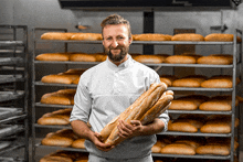 a man is holding a loaf of bread in front of a rack of bread