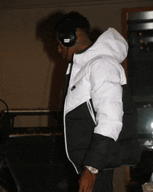 a man wearing headphones and a nike jacket stands in front of a piano