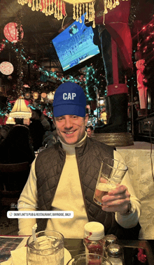 a man wearing a blue cap is sitting at a table holding a glass of beer