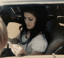 a woman is sitting in the driver 's seat of a car and looking at her phone .