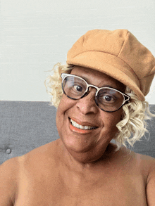 an elderly woman wearing glasses and a hat smiles for the camera