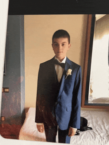 a boy in a blue suit and bow tie stands on a bed