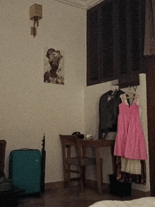 a pink dress hangs on a hanger next to a suitcase