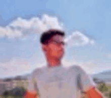 a blurry picture of a man wearing glasses standing in front of a cloudy sky .