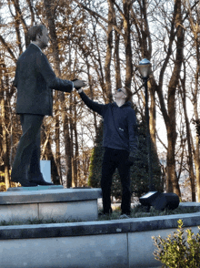 a woman reaches out to touch a statue of a man in a suit and jacket