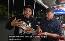 a man wearing a bulls shirt holds a plate of food next to another man