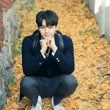 a young man in a school uniform is squatting down in a pile of leaves