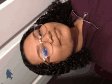 a woman with curly hair wearing glasses and a purple jacket