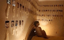 a woman is sitting on a bed in front of a wall covered in pictures of men .