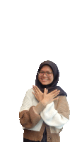 a woman wearing glasses and a hijab smiles with her hands crossed