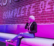 a woman sits on a couch in front of a brick wall that has the word coca cola written on it