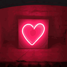 a pink heart shaped neon sign is lit up on a brick wall