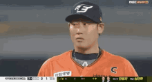 a baseball player wearing an orange jersey and a black hat is standing on a baseball field .