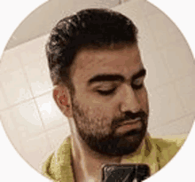 a man with a beard is taking a selfie in a bathroom with a cell phone .