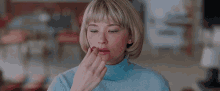 a woman with blonde hair is wearing a blue sweater and eating something