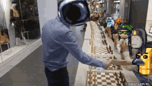 a man wearing a virtual reality headset shakes hands with another man while playing chess