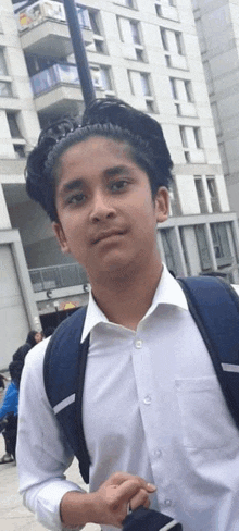 a young boy wearing a white shirt and a backpack is standing in front of a tall building .