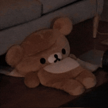 a brown teddy bear is laying on the floor near a couch