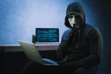 a man wearing a mask and a hoodie is using a laptop