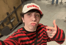 a man wearing a red and black striped shirt and a white hat that says queen