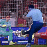 a man in a blue shirt is kicking a soccer ball at a goalie