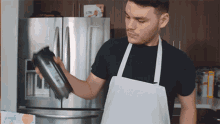 a man in an apron is standing in front of a fridge with a box of k-cups in the background