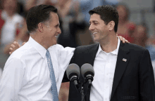 two men are standing next to each other in front of microphones and one of them is wearing a white shirt