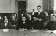 a man in a suit is giving a speech to a group of people