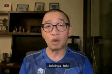 a man wearing glasses and a blue shirt is talking in a room .