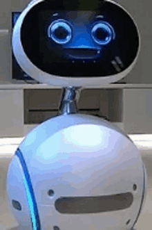 a white robot with a blue face is sitting on a table in front of a television .