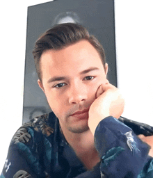 a man wearing a blue shirt with a hawaiian print has his hand on his chin