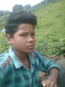 a young boy wearing a plaid shirt is sitting in a field