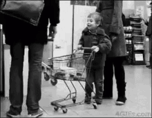 a black and white photo of a child pushing a shopping cart in a store .