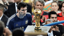 a soccer player with the number 10 on his shirt stands in front of a trophy