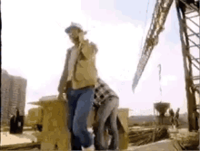 a man in a hard hat is standing next to a woman in a plaid shirt on a construction site .