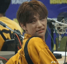 a young man in a yellow shirt is sitting in front of a microphone and making a funny face .