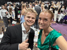 a man in a suit and a woman in a green dress give a thumbs up