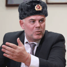 a man in a suit and tie wearing a fur hat with a red cross on it