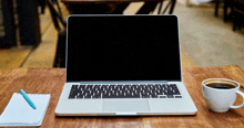 a laptop is open on a wooden table next to a cup of coffee and a notebook