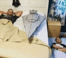 a man and a woman are laying in bed next to a model of a star destroyer from star wars