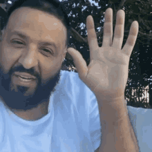 a man with a beard is sitting on a couch and waving his hand .