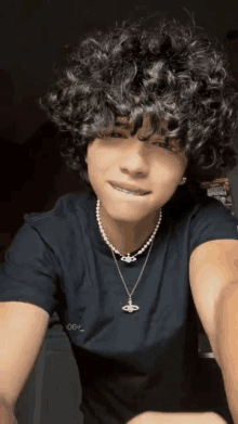 a young man with curly hair and braces is wearing a black shirt and a pearl necklace .