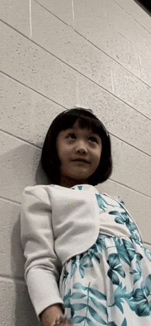 a little girl is leaning against a brick wall